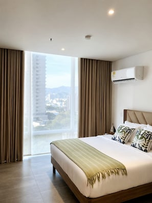 Une chambre d’hôtel avec un grand lit, un appareil de climatisation, une vue sur le paysage urbain à travers une porte coulissante et une vue sur la ville à travers une fenêtre.