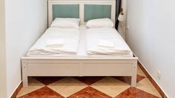A double bed with two pillows and a folded towel, a bedside lamp, and a checkered floor pattern.