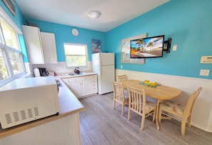 A kitchen with white cabinets, a refrigerator, a stove, and a dining table with chairs. - Resort Style, Walk to Beach & Village, Heated Pool, Tiki (Siesta Key)