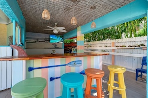 A colorful bar area with a ceiling fan, a television, and a view of palm trees. - Resort Style, Walk to Beach & Village, Heated Pool, Tiki (Siesta Key)