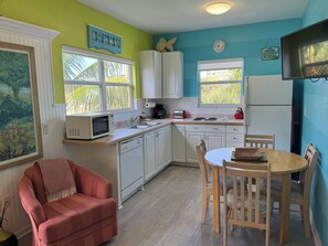 A compact kitchen with white cabinets, a microwave, a toaster, and a kettle. There is a dining table with chairs and a red chair with a throw blanket. - Old-Florida Resort, Steps to Beach & Village, Heated Pool (Siesta Key)