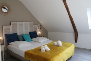 Ein Schlafzimmer mit einem Bett, Kissen, einer Nachttischlampe, einem Spiegel und einem Holzbalken.