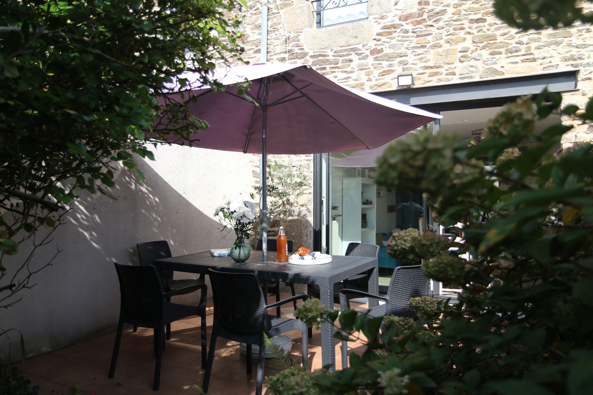 Une terrasse extérieure avec une table et des chaises, un parasol violet et un bâtiment en pierre en arrière-plan.