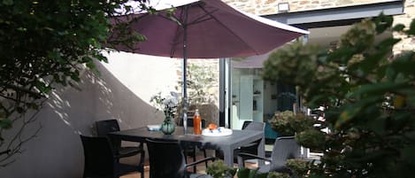 An outdoor patio with a table and chairs, a purple umbrella, and a stone building in the background.