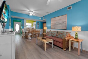 A living room with a sofa, coffee table, and a dining area with chairs and a table. - Sand & Sunsets Steps Away, Heated Pool, Village (Siesta Key)