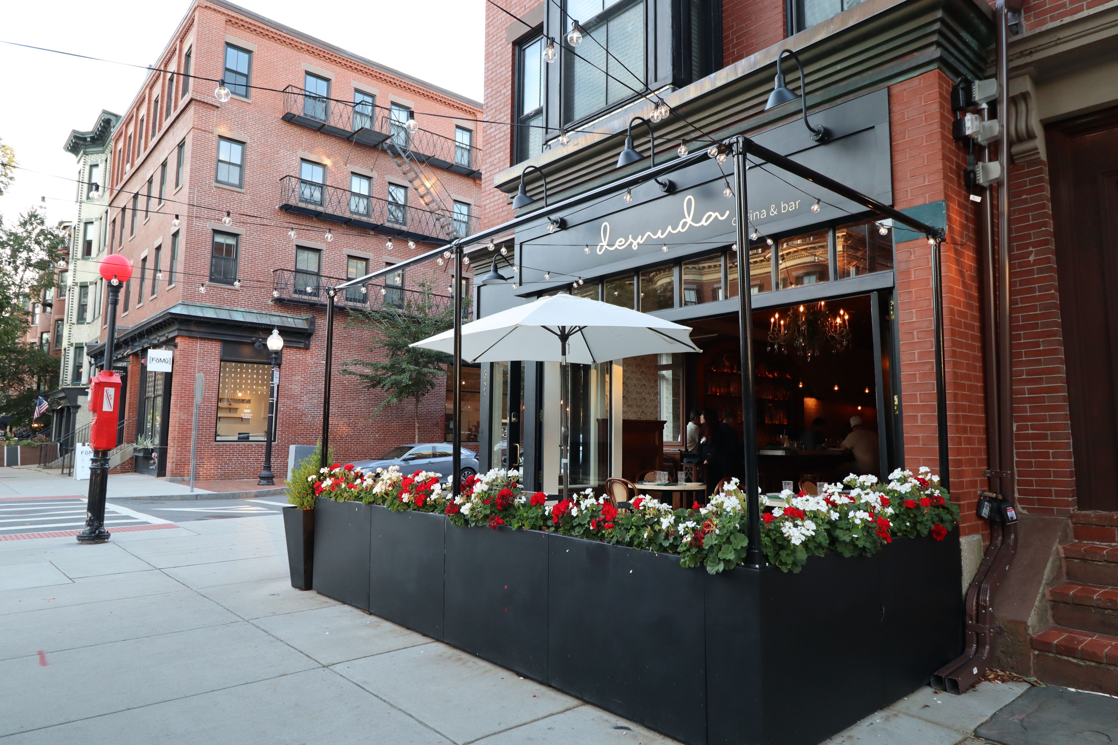 A restaurant with outdoor seating, a brick facade, and a sign reading 'Desnud.'
