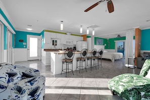 A spacious living area with a large island, a dining area with bar stools, and a bedroom with a bed and curtains. - Steps to the Sand, Walk to Village, Private Deck (Siesta Key)