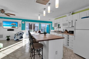 A modern kitchen with a central island, white cabinetry, and a large window overlooking a balcony. - Steps to the Sand, Walk to Village, Private Deck (Siesta Key)