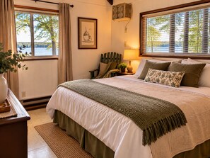 A bedroom with a large bed, a nightstand, a lamp, a framed picture, and a window with blinds. - Fabulous 2-bedroom cabin with AC in charming Talladega (Talladega)