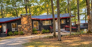 A cabin with a stone chimney, a red roof, and a deck overlooking a body of water. - Fabulous 2-bedroom cabin with AC in charming Talladega (Talladega)