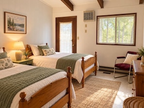 A bedroom with two wooden beds, a nightstand with a lamp, a window with blinds, and a painting on the wall. - Fabulous 2-bedroom cabin with AC in charming Talladega (Talladega)