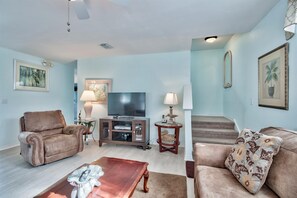 A living room with two sofas, a coffee table, a TV, and a staircase. - 🌊 A Wave From It All | Private Pool 🏊 | Golf Cart | Walk to Beach 🏖️ (Destin)