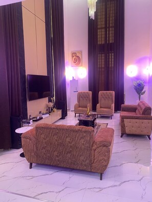 Una sala de estar moderna con una televisión de pantalla plana, dos sillones, un sofá, una mesita de centro y una planta decorativa.