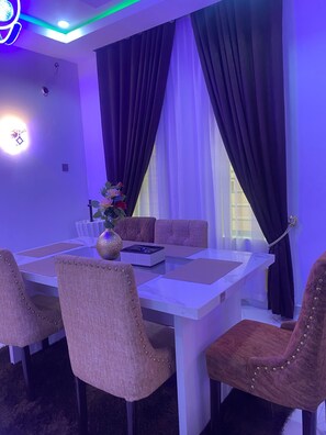 A dining area with a white table, cushioned chairs, and a vase with flowers. - Beautiful 3-bedroom apartment with AC in charming Akure (Akure)