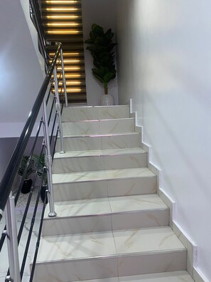 A staircase with a metal handrail, white marble steps, and a potted plant at the top. - Beautiful 3-bedroom apartment with AC in charming Akure (Akure)