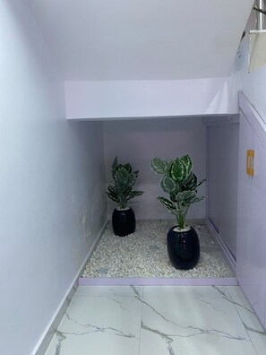 A narrow hallway with two potted plants on a pebble bed, white walls, and a tiled floor. - Beautiful 3-bedroom apartment with AC in charming Akure (Akure)