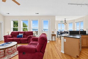 A spacious living room with a red sofa, a dining area with a table and chairs, and a kitchen with a black countertop. - Waterfront Sneads Ferry Retreat w Deck & Bar! (Sneads Ferry)