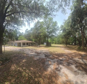 A property with a covered outdoor area, a building with multiple rooms, and a surrounding wooded landscape.