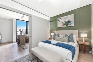 A modern bedroom with a large bed, bedside tables, a desk, and a view of the outdoors. - One Rosebank | Contemporary Comfort (Johannesburg)
