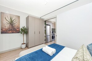Une chambre à coucher moderne avec un lit, un tapis bleu, une serviette blanche, une plante en pot et un tableau accroché au mur.