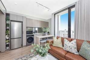 A modern apartment with a kitchen, dining area, and a living room with a brown sofa and decorative pillows. - One Rosebank | Contemporary Comfort (Johannesburg)