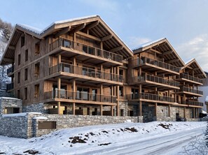 A multi-story wooden lodge with balconies, stone foundation, and snow-covered surroundings. - Reflet Des Cimes Loan Lodge (Les Belleville)