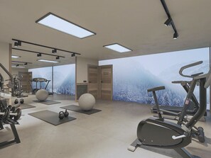 A modern gym with exercise equipment, large windows, and a view of snowy mountains. - Reflet Des Cimes Loan Lodge (Les Belleville)
