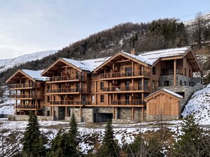 Een meerlaags houten chalet met balkons, gelegen in een besneewd berglandschap.