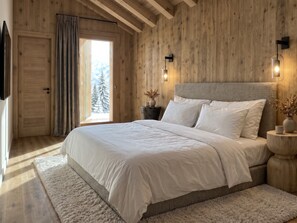 A bedroom with a large bed, wooden walls, a window with a view of trees, and a door. - Reflet Des Cimes Loan Lodge (Les Belleville)