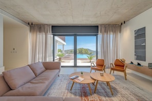 A modern living room with a sofa, two chairs, a coffee table, and a view of a swimming pool and hills. - Luxury 4-Bedroom Villa in Primošten with Private Pool & Panoramic Sea Views (Primošten)