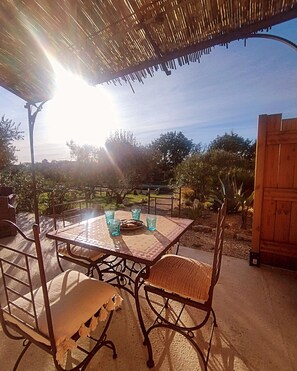 Un'area pranzo all'aperto con tavolo e sedie, un tetto di paglia e vista sul paesaggio circostante.
