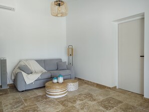 A modern living room with a grey sofa, a woven ottoman, and a pendant light fixture. - Gîte romantique 4* au calme avec jacuzzi et vue sur le piémont cévenol (Lézan)