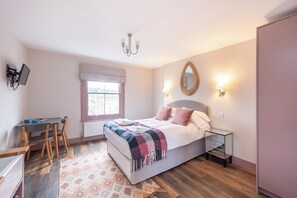 Quarto com cama, mesa de cabeceira, luminária, espelho, janela e escrivaninha com cadeira.