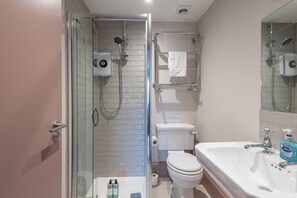 A bathroom with a glass-enclosed shower, a white toilet, and a sink with a mirror. - Wonderous Kensington Studio (London)
