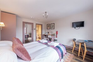 A hotel room with a bed, a desk, a chair, a television, and a bathroom visible through an open door. - Wonderous Kensington Studio (London)
