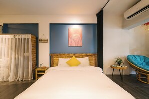 A hotel room with a bed, a wooden headboard, a wall-mounted artwork, a small side table, a chair, and an air conditioning unit. - OH Trendy homes Hoan Kiem LPH  - city center - 2 beds (Hoan Kiem)
