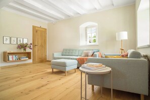 A spacious living room with a light blue sofa, a grey armchair, a wooden bookshelf, and a small round table with books. - New Listing (Nieheim)