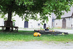 A tree-lined courtyard with a bench, a building with a door labeled 'ALTE RENTE,' and a wooden log with toys. - New Listing (Nieheim)