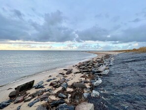 A beach with a rocky shoreline and calm sea under a cloudy sky. - Holiday Home in Nieblum With Swimming Pool (Nieblum)