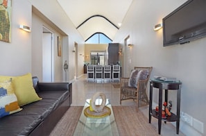 A spacious living room with a leather sofa, a glass coffee table, and a wicker chair. A flat-screen TV is mounted on the wall. - Fabulous 2-bedroom apartment in Eden on the Bay near top attractions (Cape Town)