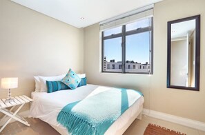 Ein Schlafzimmer mit Bett, Fenster, Spiegel und Nachttisch.