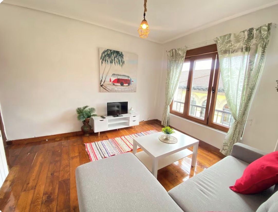 A living room with a sofa, a coffee table, a TV, and a window with curtains.