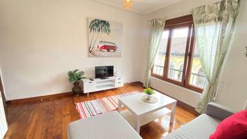 A living room with a sofa, a coffee table, a TV, and a window with curtains.