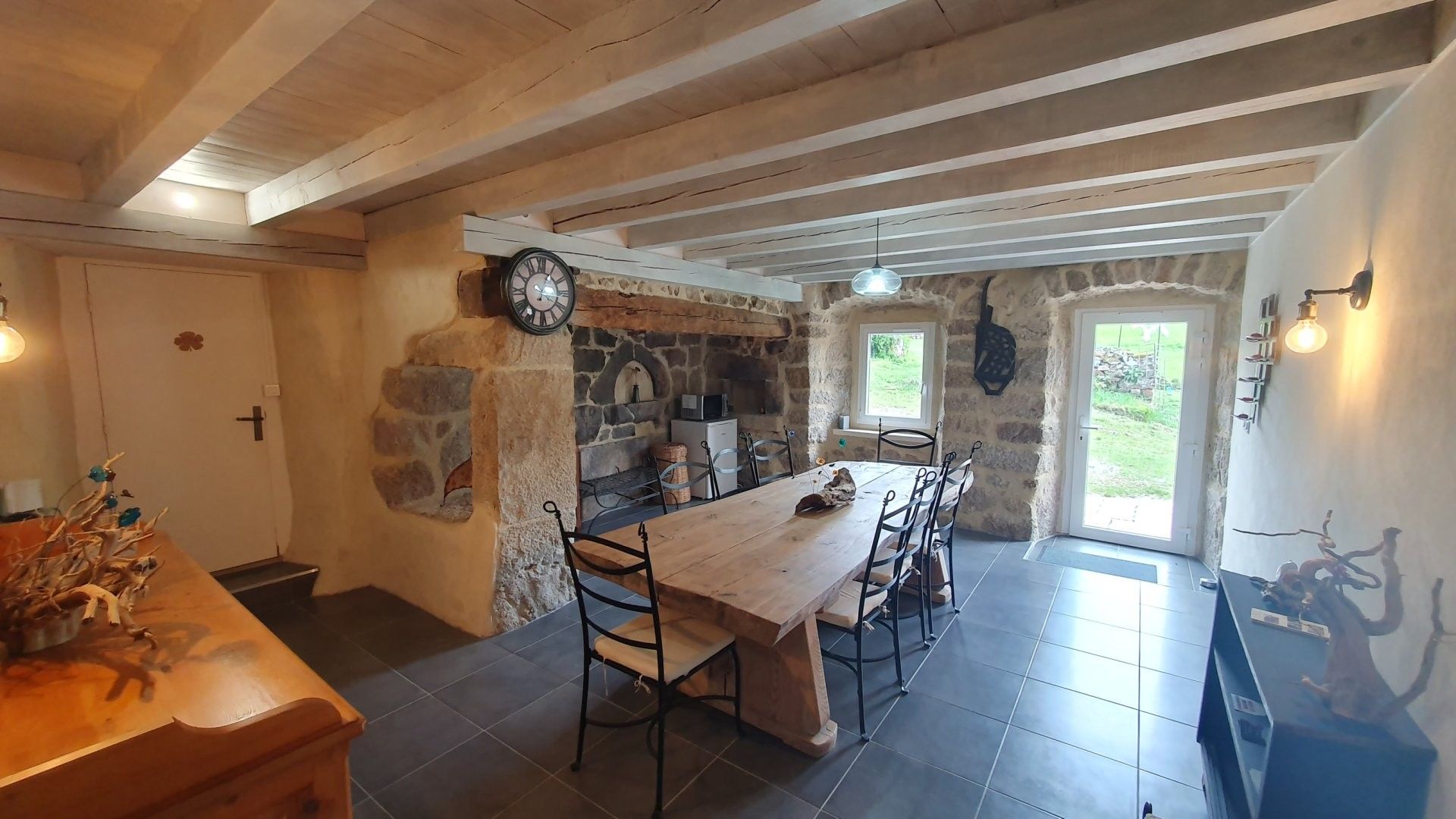 A rustic dining area with a wooden table and chairs, stone walls, and a clock.
