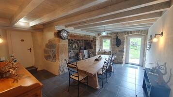 A rustic dining area with a wooden table and chairs, stone walls, and a clock.