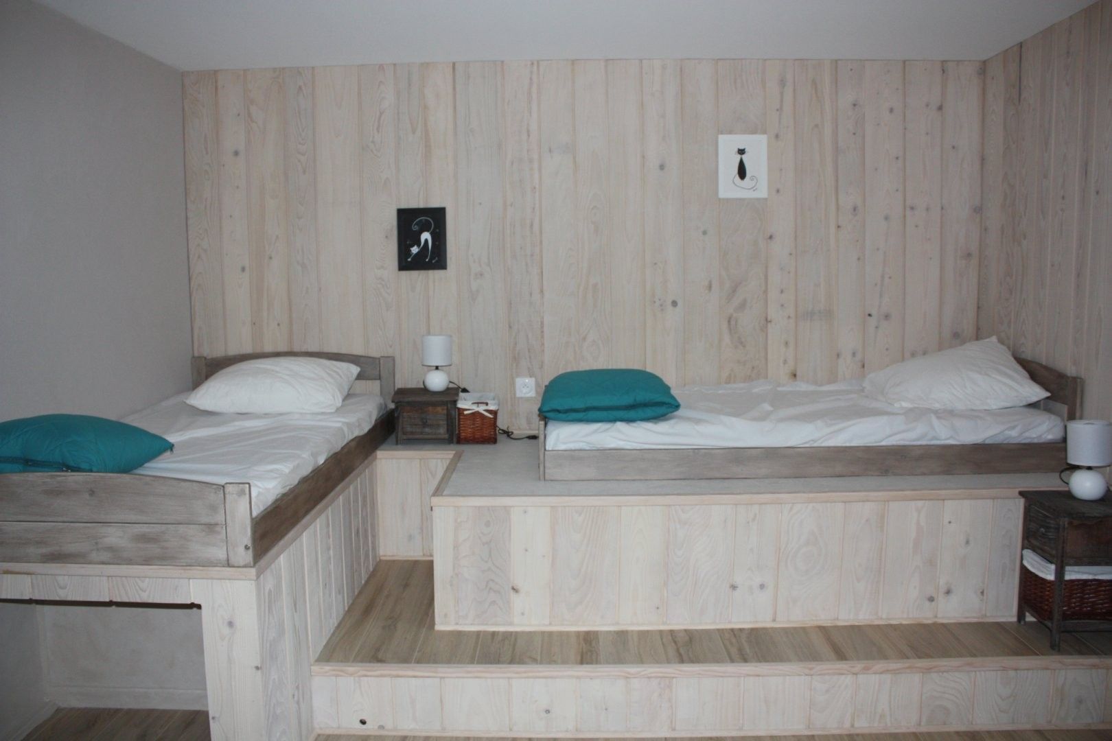 A room with two wooden beds, a small table with a lamp, and a wall-mounted picture.