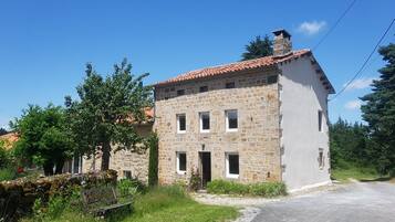 A stone building with a red-tiled roof, a small porch, and a garden with a bench.