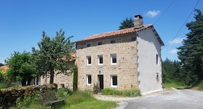 A stone building with a red-tiled roof, a small porch, and a garden with a bench.