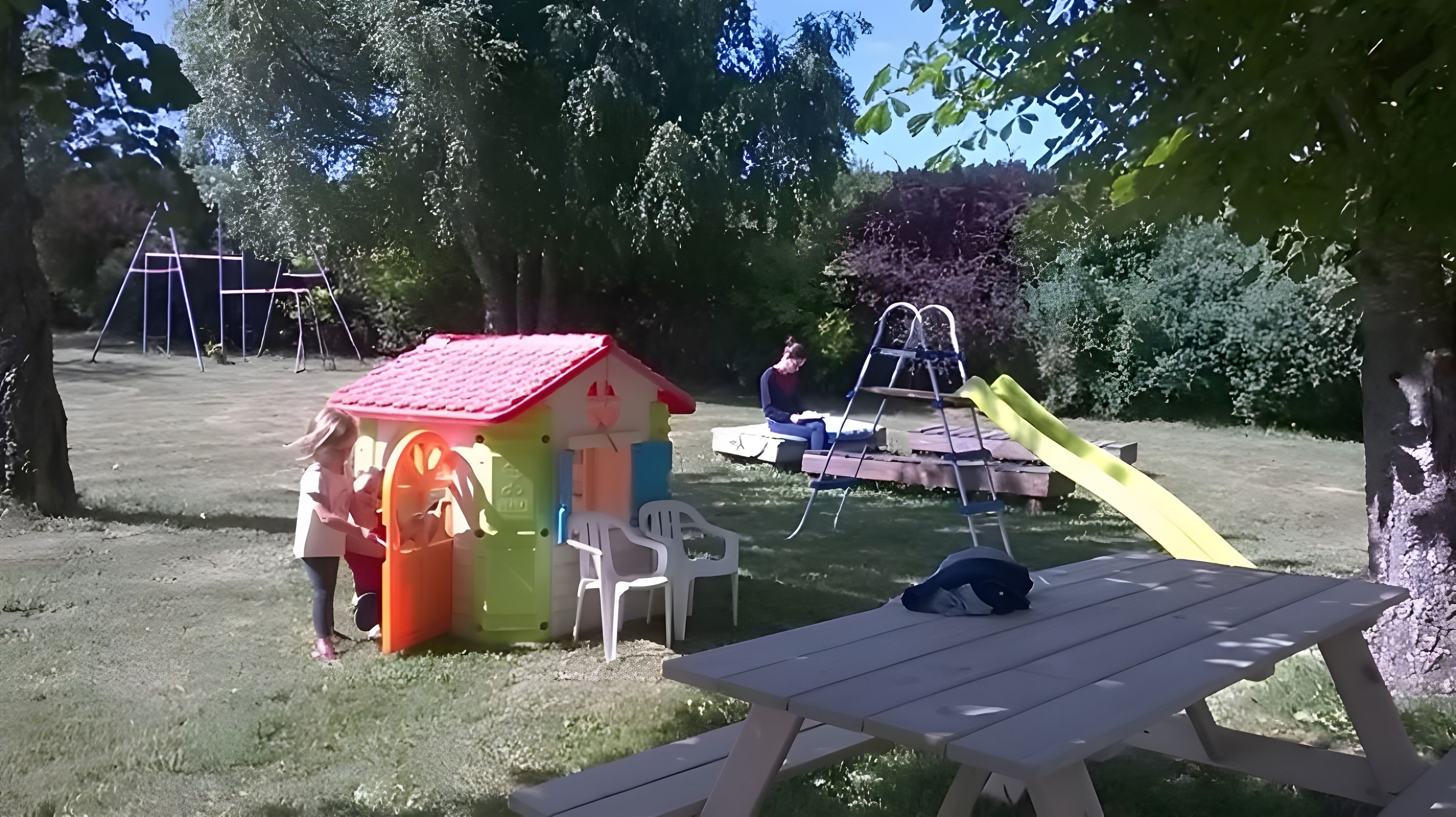 A playground with a slide, swings, and a small house.