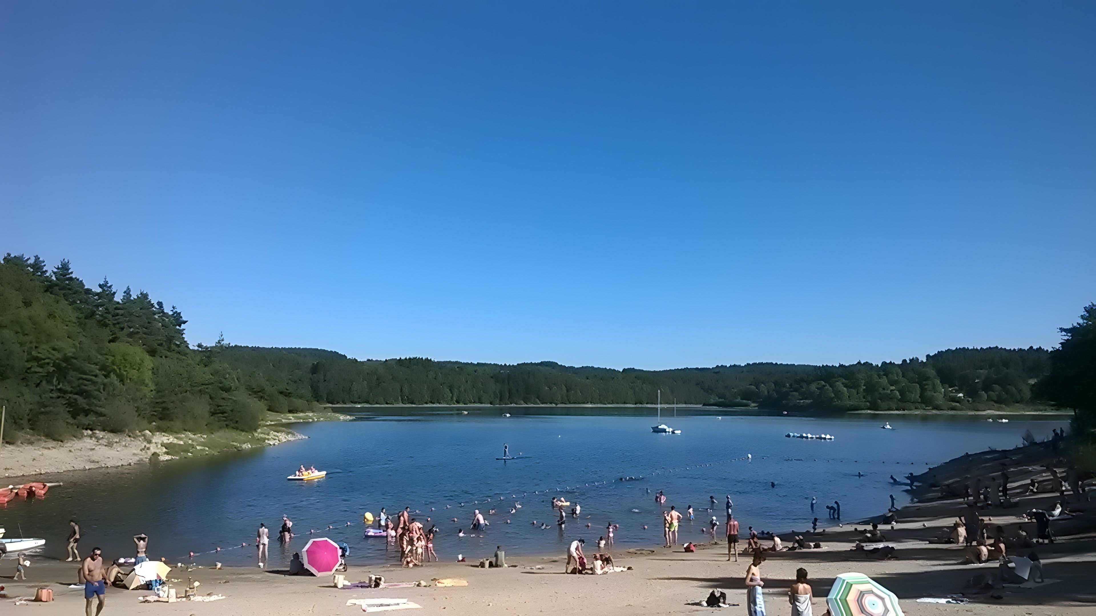 Ein Strand mit Menschen, Booten und einer bewaldeten Hügelkette im Hintergrund.